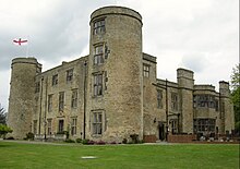 Photographie moderne d'un château comportant deux tours principale et un fronton sur lequel le drapeau de l'Angleterre flotte au vent.