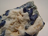 A rough rock showing several intense, dark blue benitoite crystals emerging from white natrolite matrix.