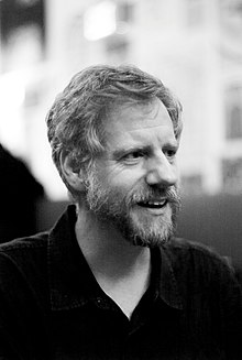 black-and-white image of Michael W. Carroll, wearing a black shirt, looking left of camera, appearing to grin