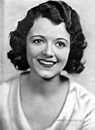 The sepia-toned image of a smiling female. She is wearing a light-colored blouse.