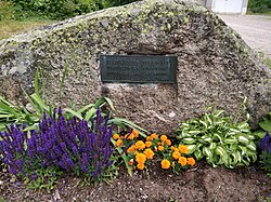 Kivi, jossa muistolaatta ja jonka edessä kasvaa kukkia.