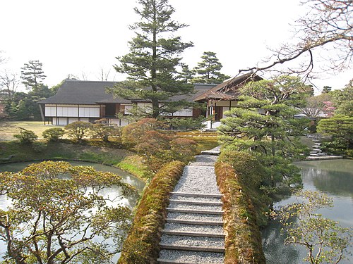 Villa impériale de Katsura. Pont, depuis le pavillon de thé Shokatei. À gauche : le Nouveau Shoin. Derrière le grand pin : Shoin Intermédiaire, espace correspondant à la salle des audiences. Entre les deux premiers : salon de musique (ouverture obscure). À droite du grand pin : véranda qui donne sur la Terrasse de la Lune (masquée par le pin tors) et donnant accès à l'Ancien Shoin, dans une antichambre.