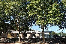 Photographie en couleur de l'entrée d'un stade, bordée d'arbres.