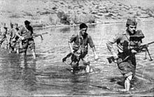 Des hommes en arme traversant à pied un cours d'eau.