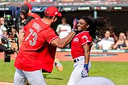 Une femme et un homme en tenue de baseball se tapent dans la main avec de l'élan devant les caméras de télévision.