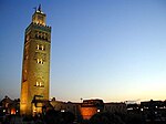 A ground view of an artificially lit tower, reaching several storeys high, at the beginning of a sunset.