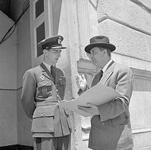 Un homme d'une cinquantaine d'années, en civil, discutant avec un très jeune homme en uniforme.