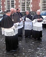 Enkele kanunniken van het Sint-Salvatorskapittel te Brugge. Zij dragen een zwarte soutane met zwarte sjerp, superplie, zwart mozetta met paarse zoom en paarse knopen.