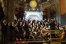 Soloists left, orchestra and choir on risers at a Baroque church