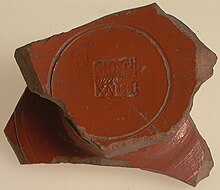 Photographie d'un fragment de céramique à l'engobe rouge portant la marque d'un potier.