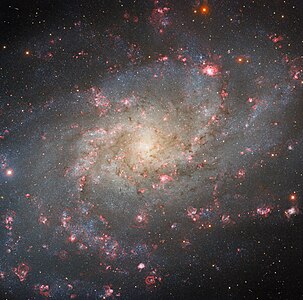 アメリカ合衆国アリゾナ州キットピーク国立天文台にある Nicholas U. Mayall 4-meter Telescope で撮影された、渦巻銀河M33。赤い斑点のように見える部分はHII領域で、内部では盛んな星形成が行われている。銀河中心の右上に一際大きく見える赤い塊がNGC 604である。