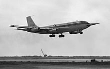 Vue latérale d'un avion volant de la gauche vers le droite de l'image ; une longue perche est visible sur la pointe avant ; le train d'atterrissage est sorti et la piste est visible en-dessous.