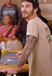 A man with tattoos covering his left arm looks to his right while playing poker.