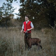 The cover artwork for "Rim Tim Tagi Dim". The cover features Marko Purišić in a white shirt and red vest standing with a cane in a grassy setting. To his left, a goat stands nearby him.