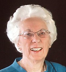 Photo of an elderly Pat Marsh with white hair, eyeglasses, pearl necklace, and blue shirt