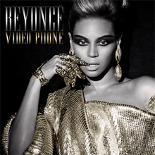 Beyoncé wearing a golden cloth with bare left shoulders. Her right hand is held across her right cheek, and she wears a number of golden rings and metallic contraptions around her fingers. She has dark make-up around her eyes and her hair is pulled back on the top.