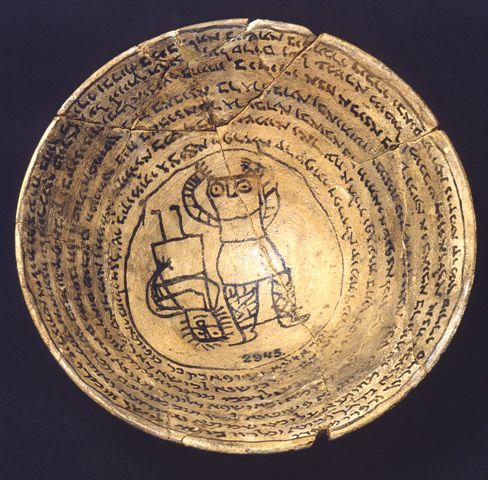 A ceramic bowl with text around the rim, and a line drawing of two figures in the middle, one raising their arms up, the other upside-down and with a funny smile