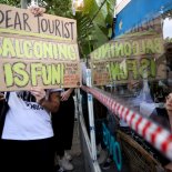 Article thumbnail: A tourist watches as demonstrators protest against mass tourism in Barcelona, Spain, July 6, 2024. The Catalan capital received more than 12 million tourists in 2023 and expects more in 2024. REUTERS/Bruna Casas