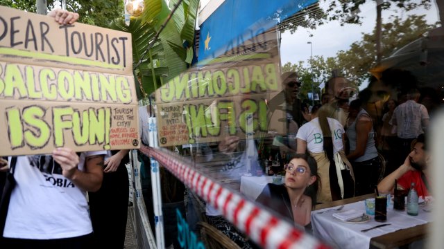 Article thumbnail: A tourist watches as demonstrators protest against mass tourism in Barcelona, Spain, July 6, 2024. The Catalan capital received more than 12 million tourists in 2023 and expects more in 2024. REUTERS/Bruna Casas