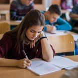 Article thumbnail: Female high school student writing during a lecture at school. There are people in the background.