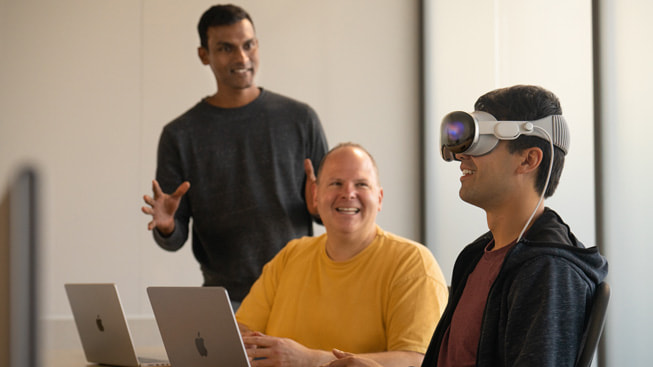 Bir geliştirici Apple Vision Pro’yu test ederken onu izleyen iki geliştiriciyle birlikte gösteriliyor.