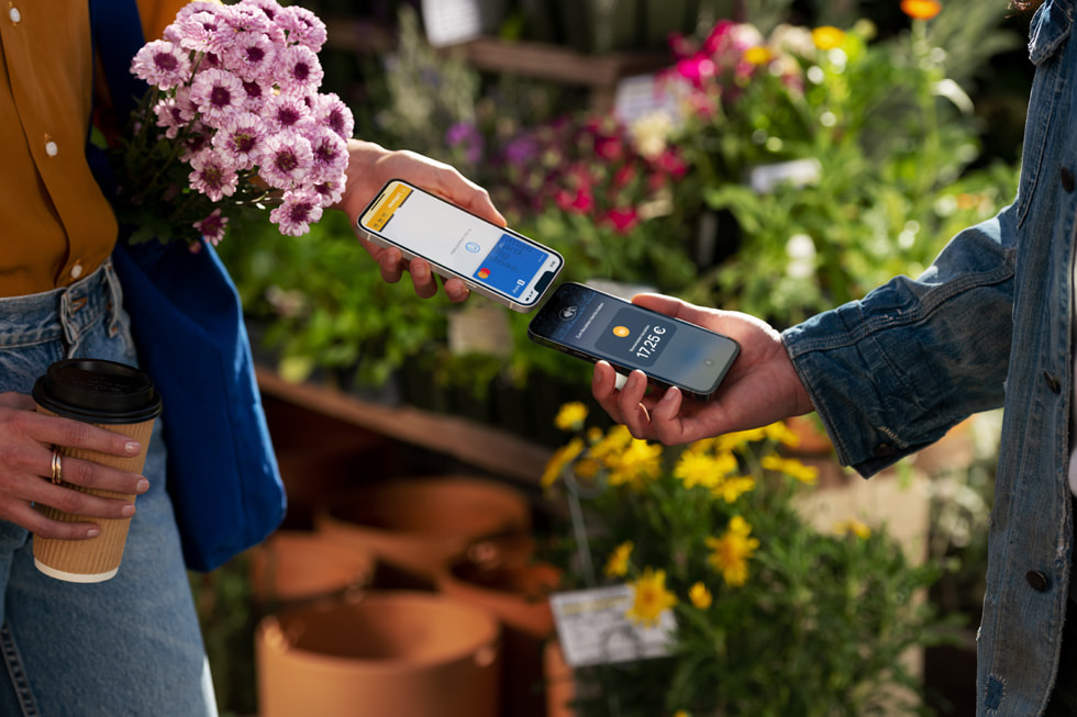 Eine Kundin mit Blumen hält ihr iPhone neben das iPhone eines Händlers, um die Transaktion abzuschließen.
