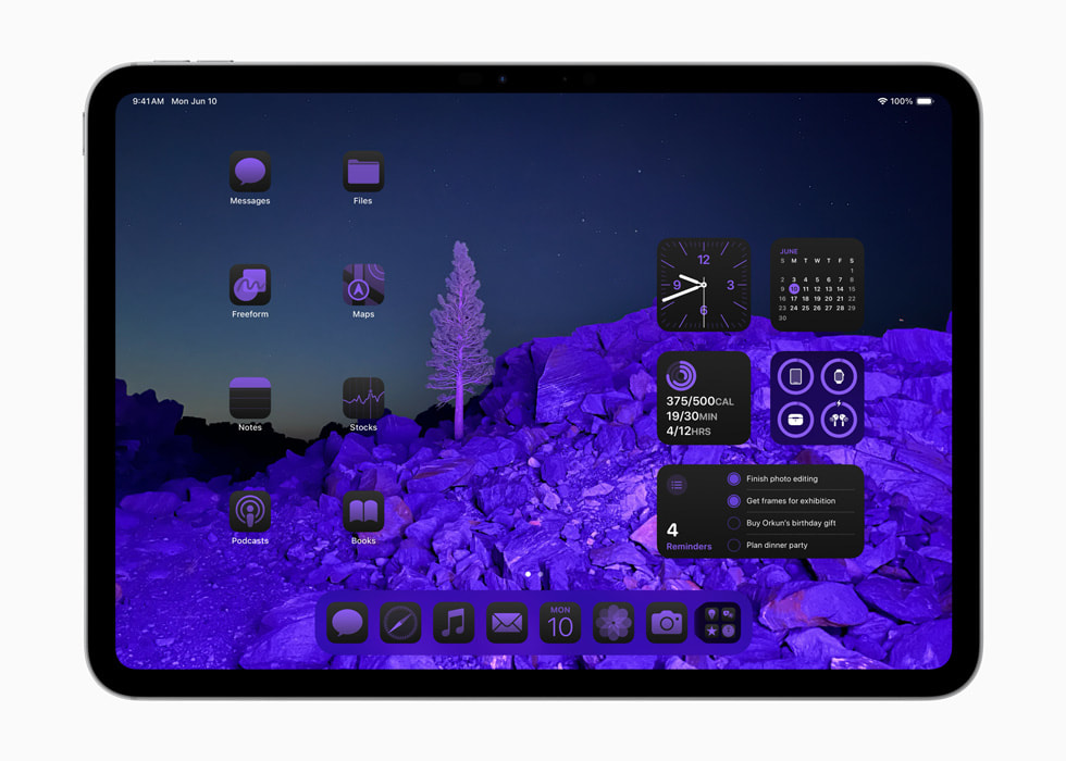 iPad Pro montrant les icônes d’apps et les widgets disposés autour d’un fond d’écran représentant un paysage, le tout teinté de violet. 