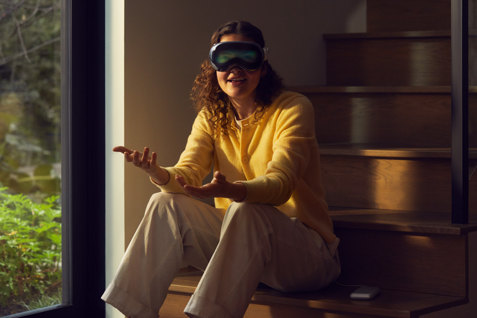 A person sitting on their steps at home having a conversation with Apple Vision Pro.