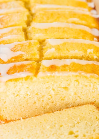 Sliced lemon loaf cake with white glaze on a wooden surface.