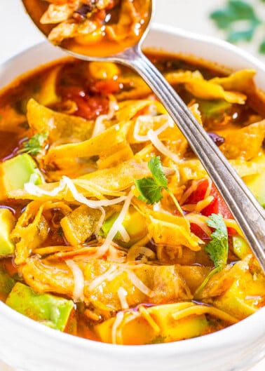 A close-up of a hearty bowl of vegetable soup with a spoon lifting a portion, showcasing vibrant vegetables and a garnish of fresh herbs.