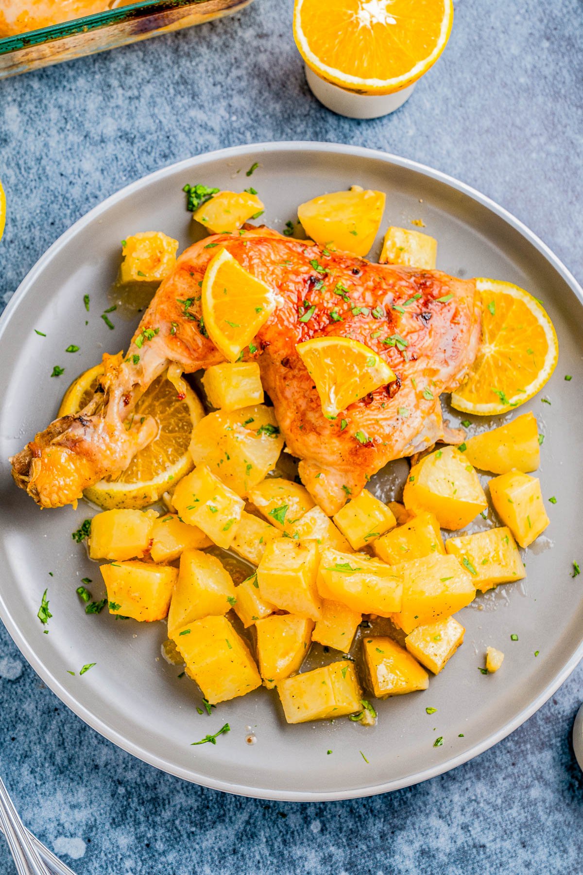 Roast chicken leg and diced potatoes on a plate, garnished with orange slices and herbs.