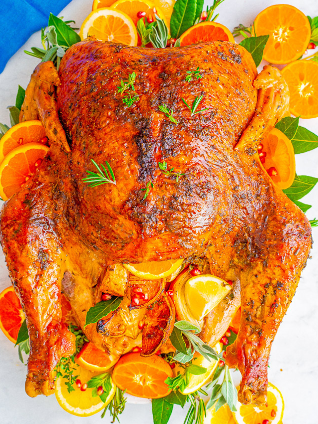 Roasted turkey garnished with orange slices, fresh herbs, and lemon wedges on a white surface.