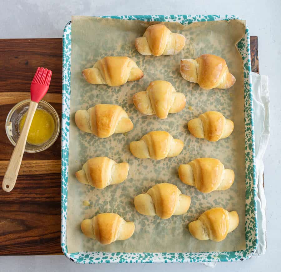 top view of the freshly baked small shiny buttered rolls in a rolled up croissant shape on a baking sheet