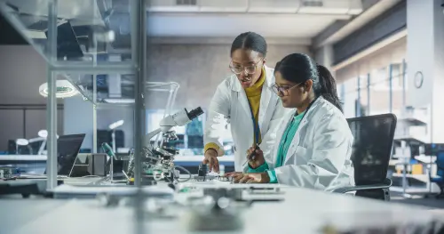 Indian Girl Having a Conversation with a Mentor in a Laboratory, While Working on a Circuit Board for a Project. Young Scholar Talking with a Scientist About Changing the CPU Memory Characteristics