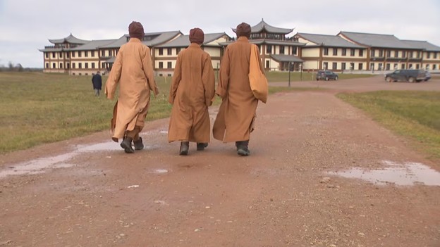 Three monastics walking toward a building on a dirt path