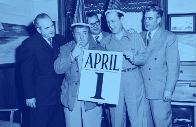 two men in party hats hold a giant calendar page reading "April 1st"