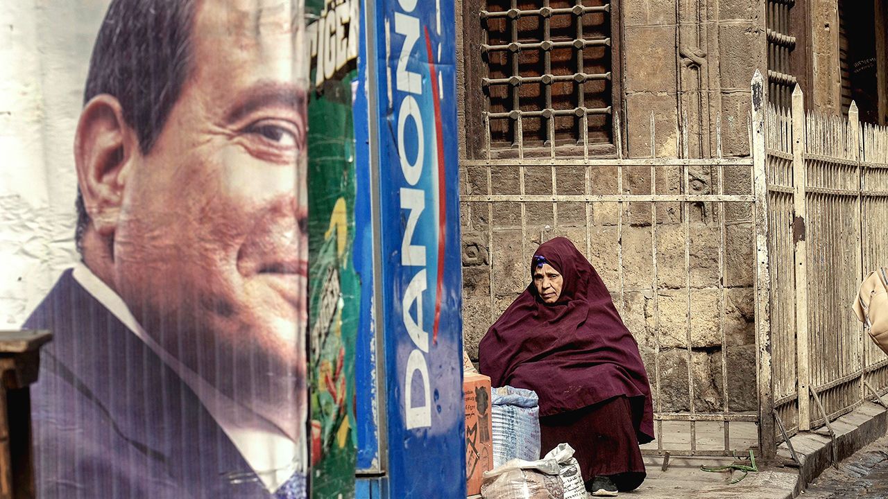 An Egyptian vendor sits behind half of a poster of Abdel-Fattah al-Sisi, the Egyptian president, in Cairo