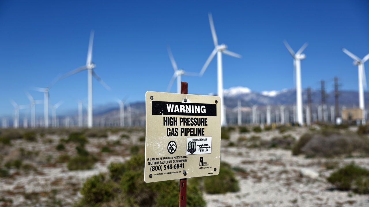 Wind turbines operate at a wind farm in Palm Springs with a sign in the foreground reading 'Warning - Gas pipeline' in California, USA.