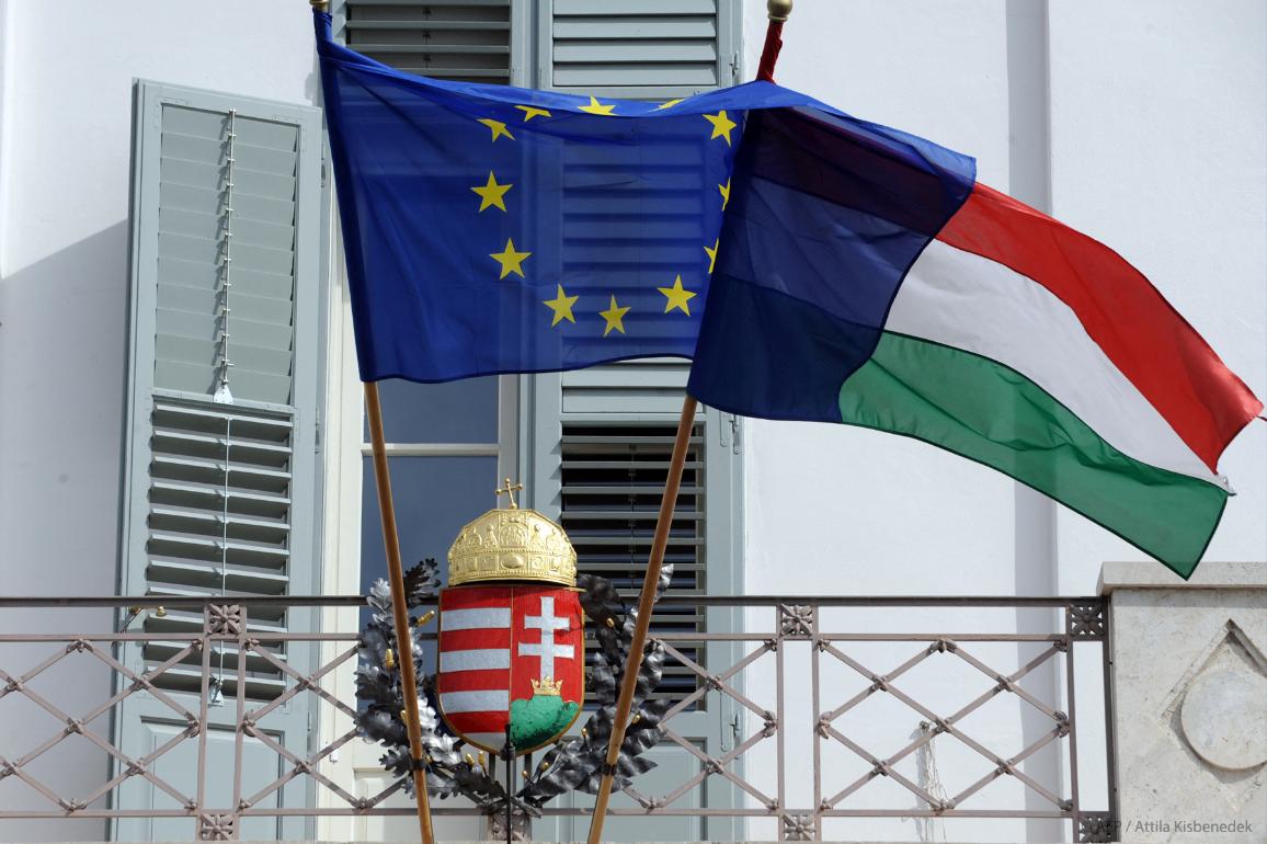 EU and Hungarian flags fly in front of a Hungarian crest.