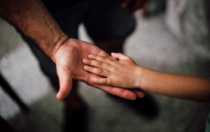 Adult hand extended and open to hold a child's smaller hand, palm facing palm