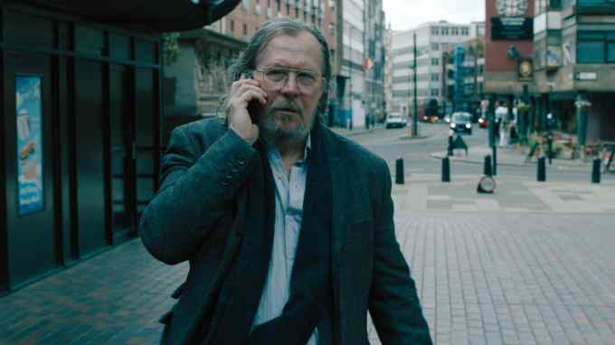 A dishevelled man with a beard in a suit looks harried or worried on the phone in a London street