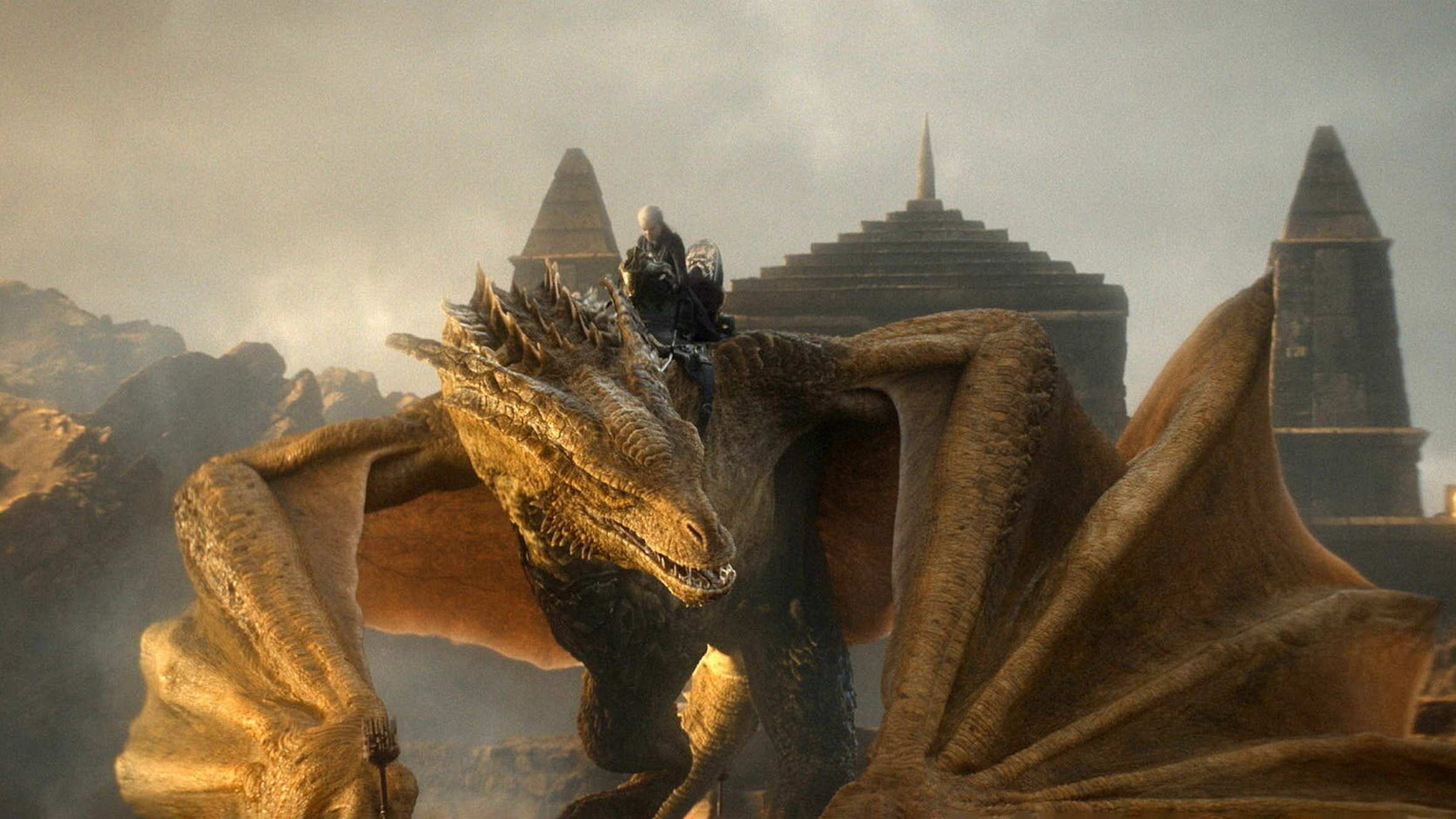 A person with white-blond hair rides on a huge dragon, with the roofs of temple-like buildings behind