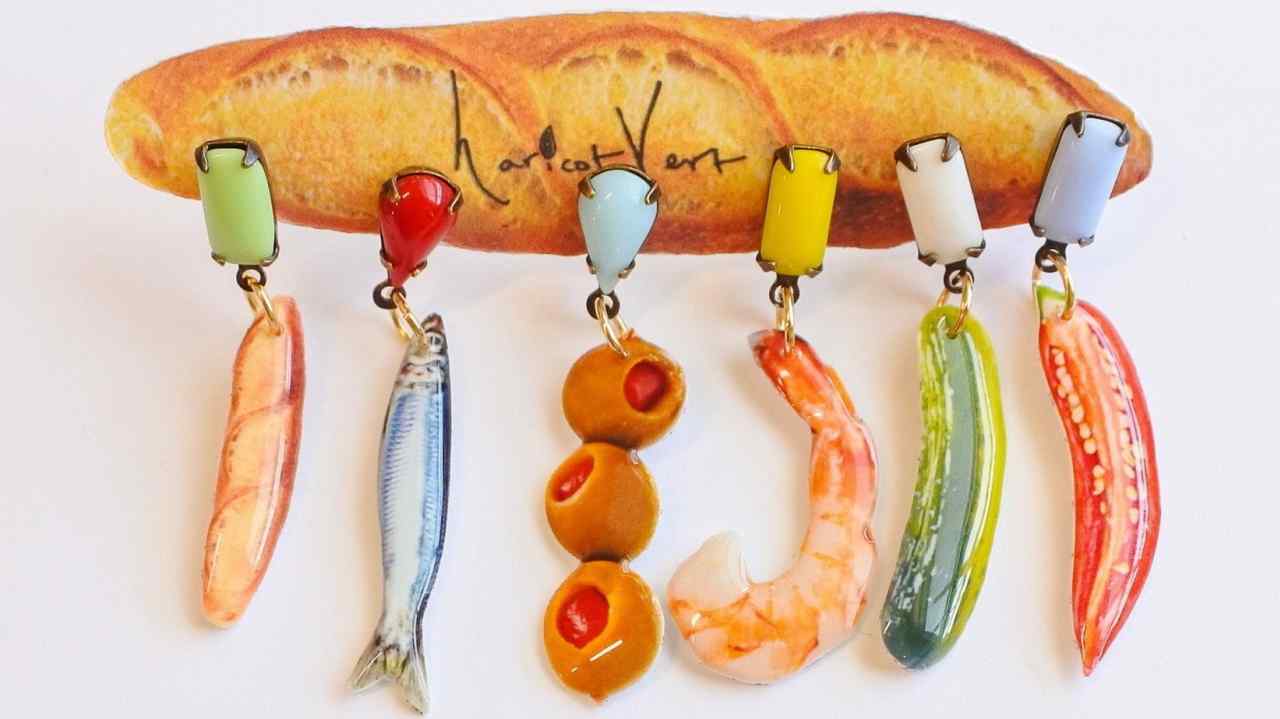 Earrings shaped to look like a sardine, a shrimp, some olives and so on, dangle from a baguette loaf