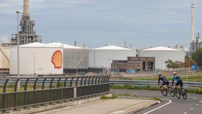 Cyclists ride past oil storage silos at the Shell Plc Pernis refinery in Rotterdam