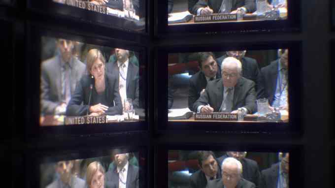 Two lines of monitors show an image of Samantha Power seated at a table with a microphone in front of a name plate displaying with the words ‘United States’ on one side. The other side shows an image of Vitaly Churkin in front of a name plate that says ‘Russian Federation’.