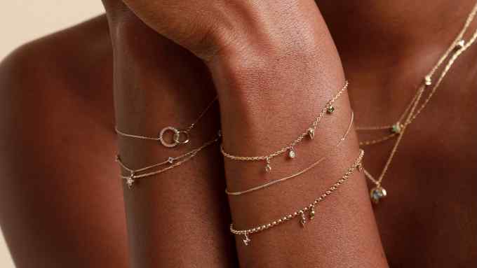 A close-up of a woman’s arms adorned with multiple delicate gold bracelets featuring small charms and gemstones