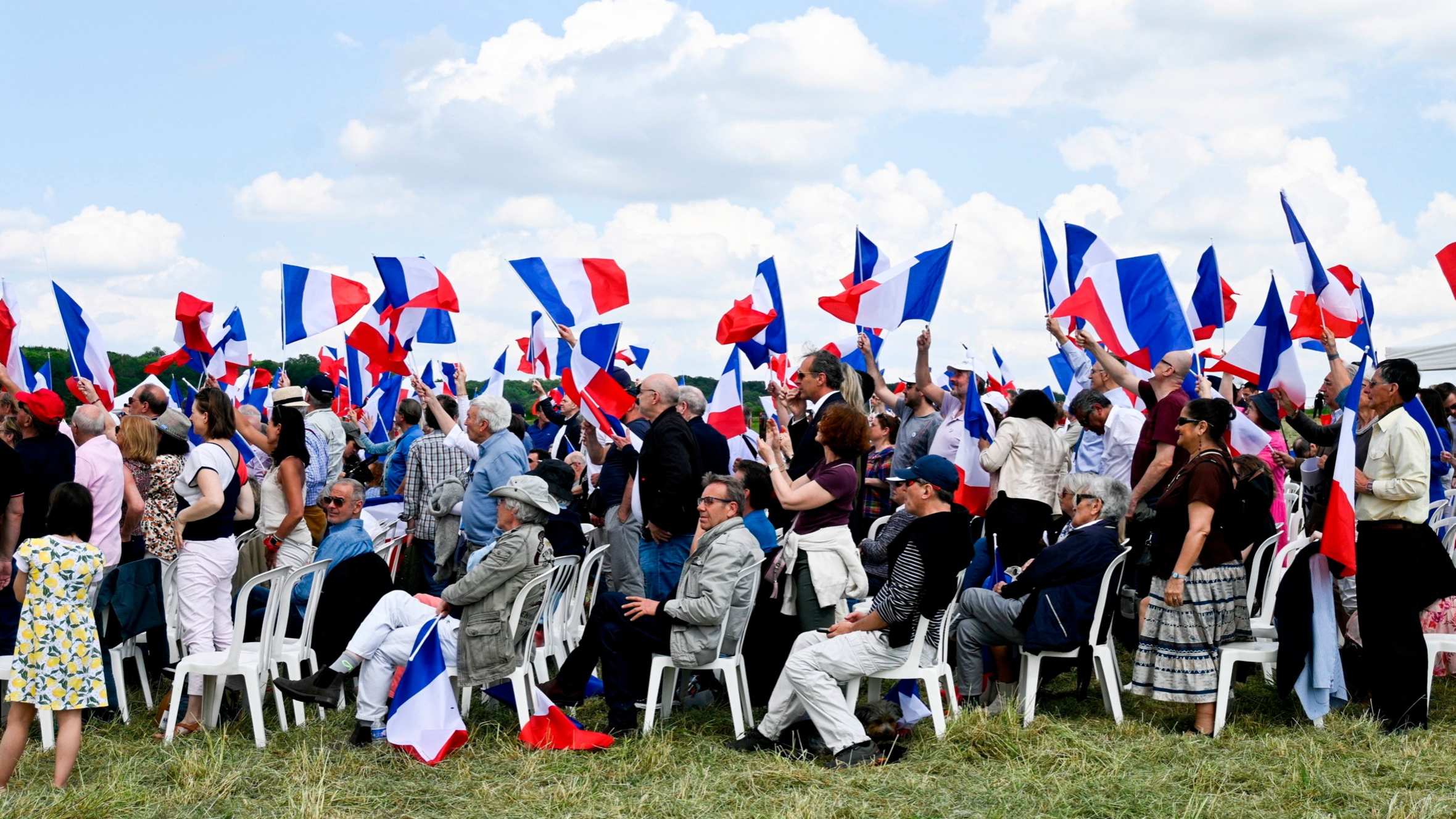 A group of people sit or stand on the grass waving French flags