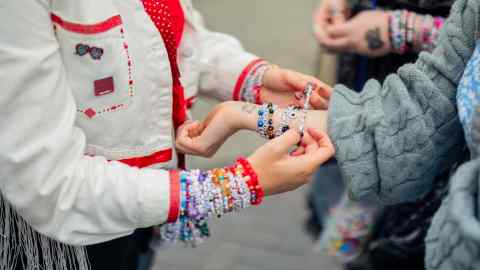 A group of individuals participating in a bracelet exchange. The focus is on their hands and wrists, which are covered in vibrant, beaded bracelets