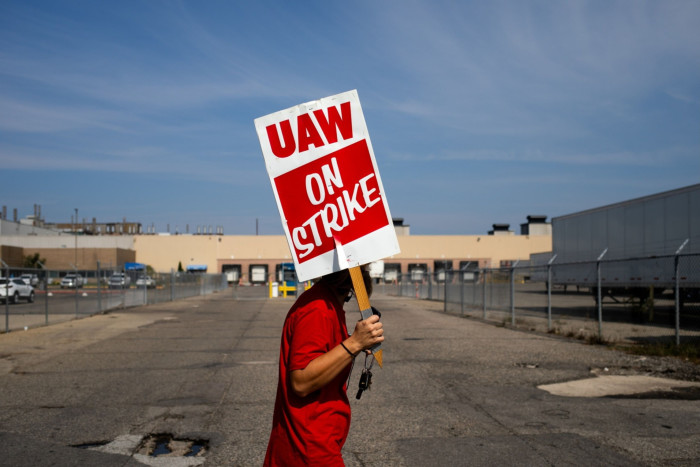 A man outside a factory holding a placard saying UAW on strike