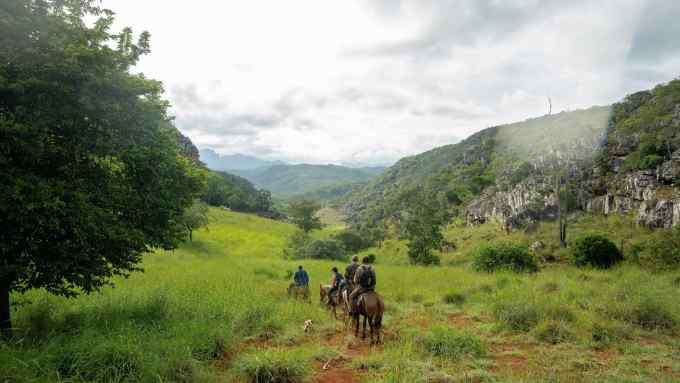 People on horseback ride through the floor of a lush green valley